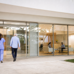 Fachada genérica de hospital particular com equipe de saúde e pacientes em área de atendimento, sem logotipos ou textos legíveis