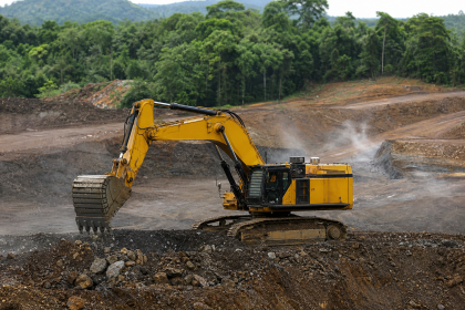 Escavadeira hidráulica em área de mineração cercada por vegetação