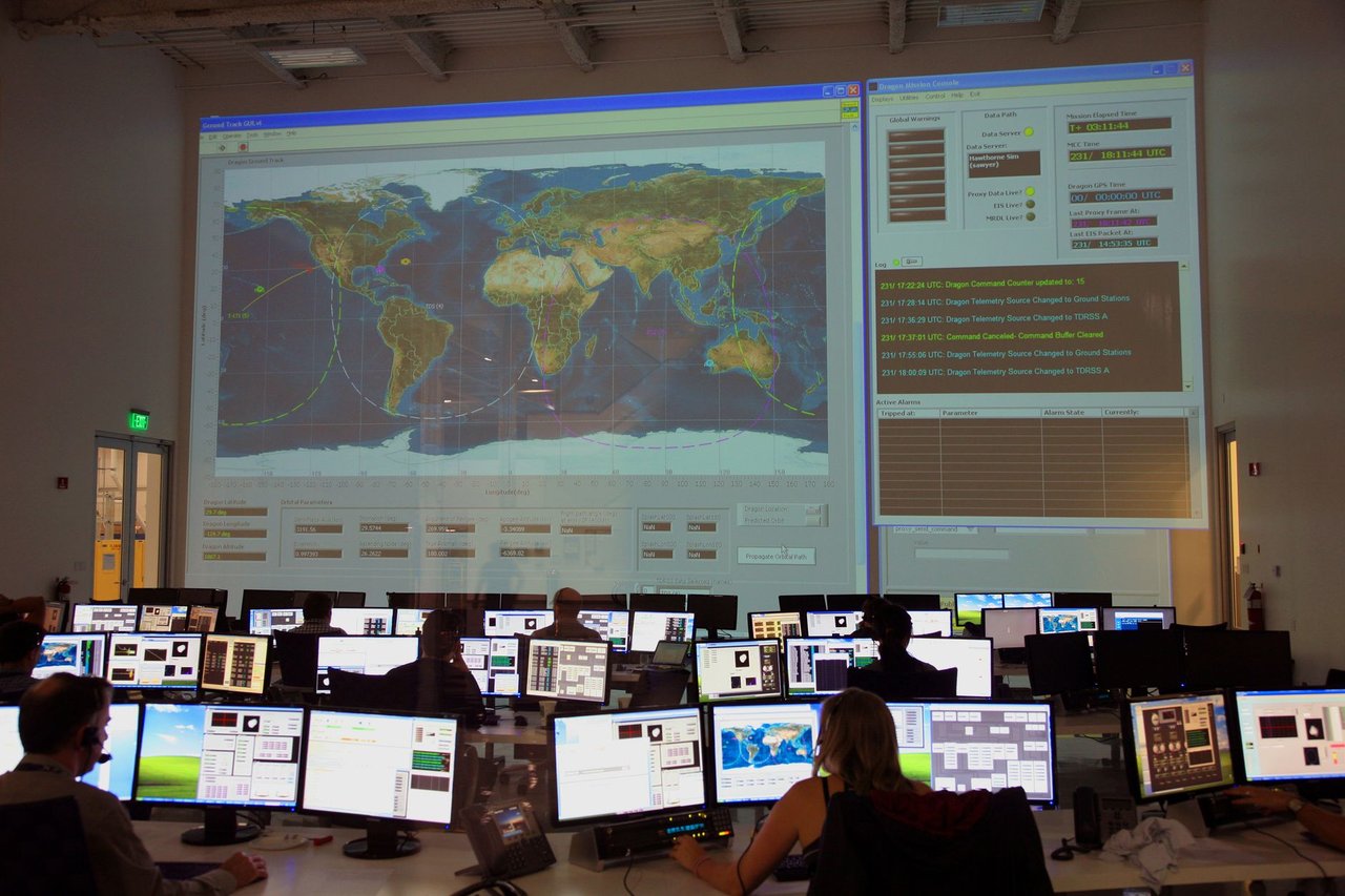 Profissionais analisam dados diante de computadores e de um grande mapa interativo em uma sala de controle.