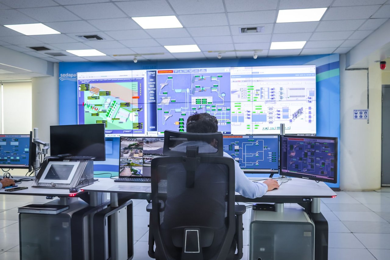 Operador acompanha sistemas em uma moderna sala de controle, diante de painéis e telas de monitoramento