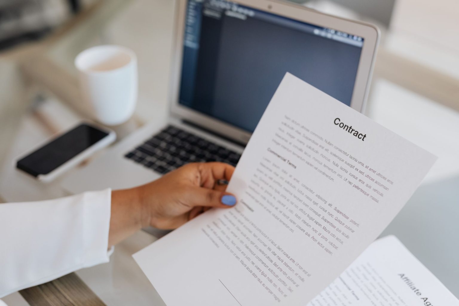 Pessoa segurando um documento jurídico ao lado de um laptop em um ambiente de trabalho.